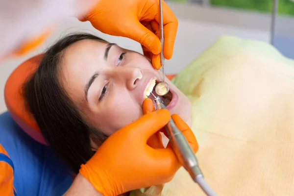 Young  woman having tooth drill procedure at dental office. Over the shoulder view on girl with open mouth.