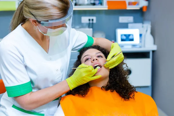 Orta yaşlı beyaz bir kadından diş kontrolü alan güzel melez bir genç kız. Coronavirus güvenlik önlemi dişçinin ofisinde. 
