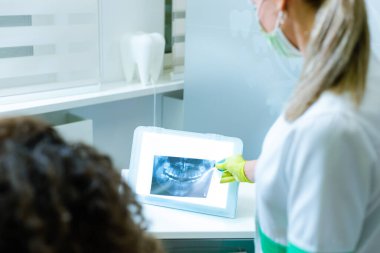 Kadın dişçi, genç kız hastasına röntgen ve çene röntgenini gösteriyor.)