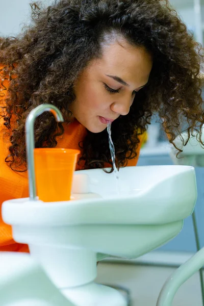 Teenage girl rinse mouth after treatment at dental office, spitting water in cuspidor - ceramic bowl