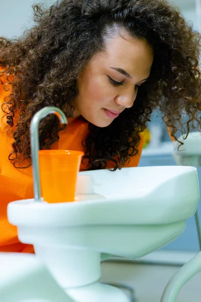 Teenage girl rinse mouth at dental office, spitting water in cuspidor - ceramic bowl