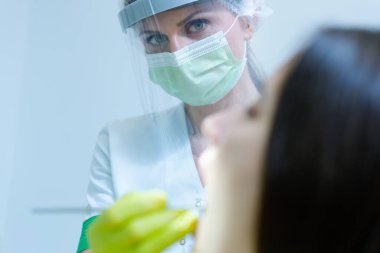 Coronavirus güvenlik önlemi olarak yüz maskesi ve vizörü olan güzel kadın diş hekimi genç bayanın diş sağlığı kontrolü