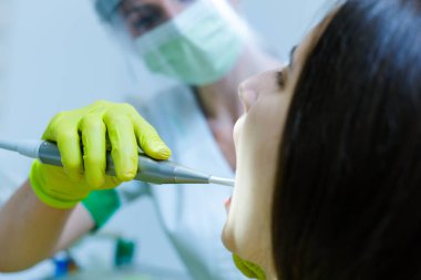 Coronavirus güvenlik önlemi olarak yüz maskesi, eldiven ve güneşlik takan kadın diş hekimi.