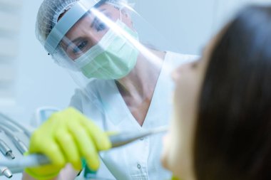 Coronavirus güvenlik önlemi olarak yüz maskesi ve vizörü olan kadın dişçi.