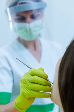 Coronavirus güvenlik önlemi olarak yüz maskesi ve vizörü olan kadın dişçi kadın diş sağlığı kontrolü