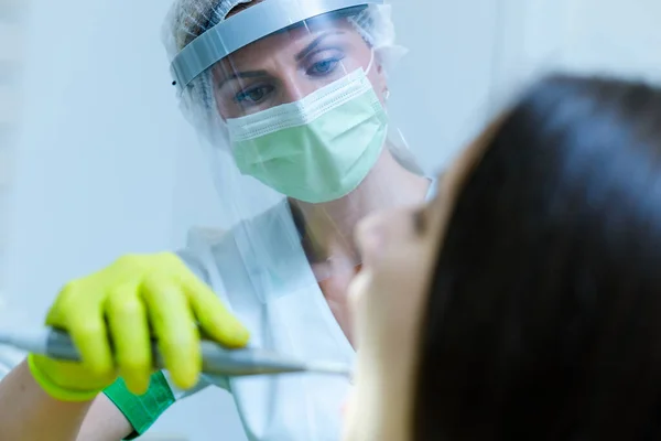 Coronavirus güvenlik önlemi olarak yüz maskesi ve vizörü olan kadın dişçi.