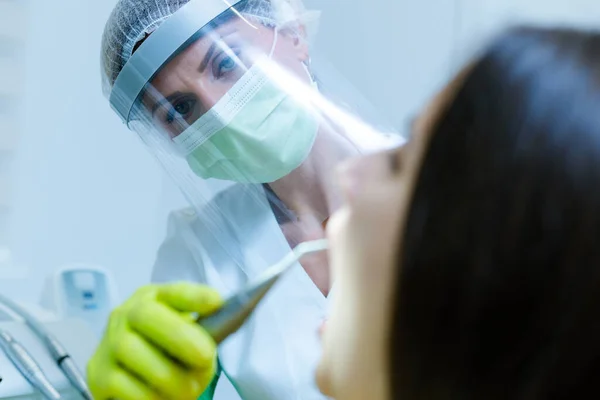 Coronavirus güvenlik önlemi olarak yüz maskesi, eldiven ve güneşlik takan kadın diş hekimi.