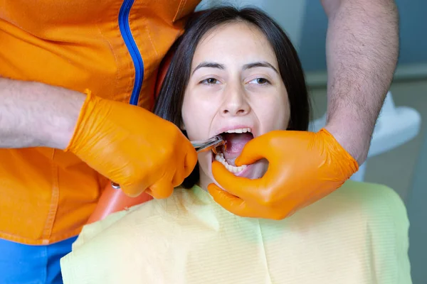 Male dentist using forceps to remove bad tooth out of young female patient.