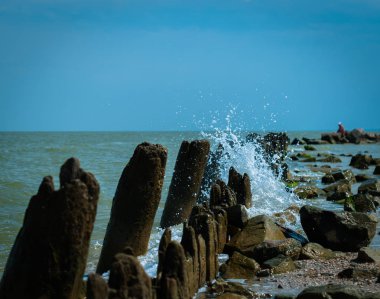 Güneşli yaz gününde birçok damla ve eski iskele ahşap kalıntıları ile bir deniz dalgası 