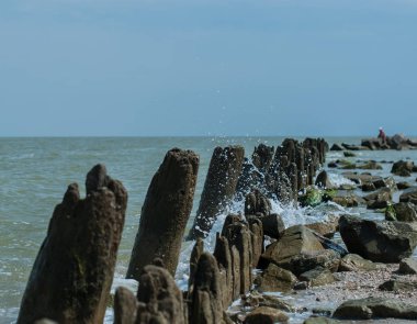 Güneşli yaz gününde birçok damla ve eski iskele ahşap kalıntıları ile bir deniz dalgası 