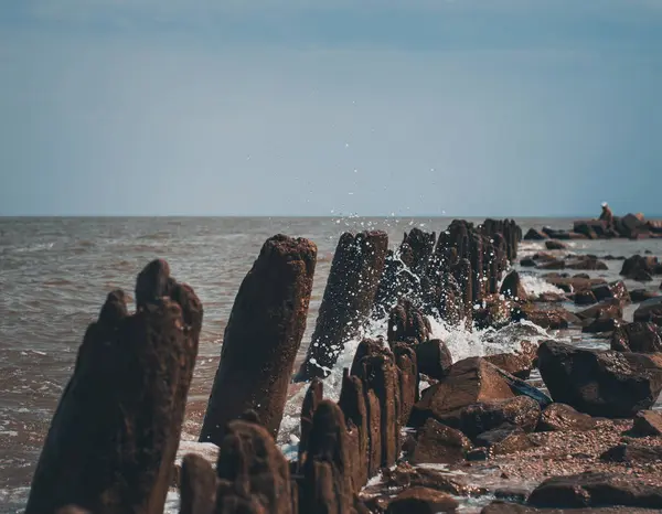 Güneşli yaz gününde birçok damla ve eski iskele ahşap kalıntıları ile bir deniz dalgası 