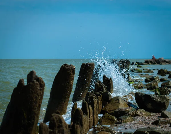 Güneşli yaz gününde birçok damla ve eski iskele ahşap kalıntıları ile bir deniz dalgası 