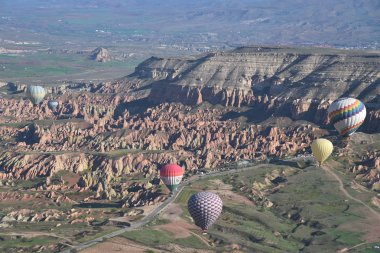 Kapadokya, Türkiye'de sıra dışı kayalık manzaranın panoramik manzarası. Renkli sıcak hava balonları Kapadokya bölgesinin derin kanyonları, vadileri ve peri bacaları üzerinde gökyüzünde uçuyor. 