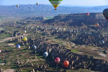Kapadokya, Türkiye'de sıra dışı kayalık manzaranın panoramik manzarası. Renkli sıcak hava balonları Kapadokya bölgesinin derin kanyonları, vadileri ve peri bacaları üzerinde gökyüzünde uçuyor. 