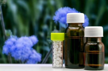 Gelişmiş Homeopatik Konsept - Bulanık mavi çiçek ve yeşil yaprakları arka plan ile cam şişehomeopatik globule şeker hapları ve sıvı madde görüntü kadar yakın