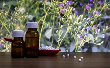 Kırmızı kaşık ve yabani çiçek arka plan ile ahşap yüzeyinde bazı dağınık globüller ile sıvı madde şişeleri homeopatik hapların yakın çekim görüntüsü.