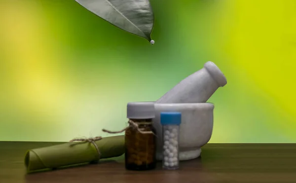 A mortar, homeopathic pills medicine bottles with rolled leaf and Homeopathic globule on the tip of a green leaf on green mix green background. A homeopathy concept