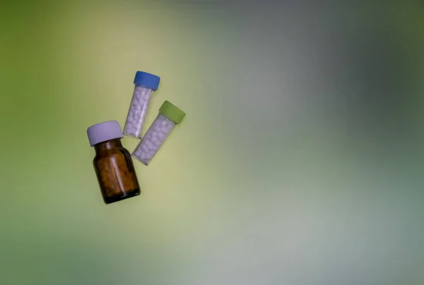 Close up of homeopathic medicine bottles containing pills on mix green yellow background. Medicine and treatment concept