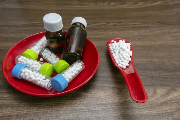 Close view image of Homeopathic medicine substance bottles in red plate and pills in red spoon on wood background.