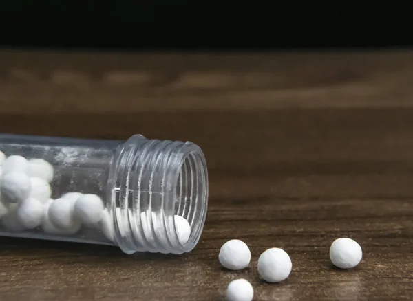 A bottle of homeopathic pills scattered on wooden surface. Medical health concept