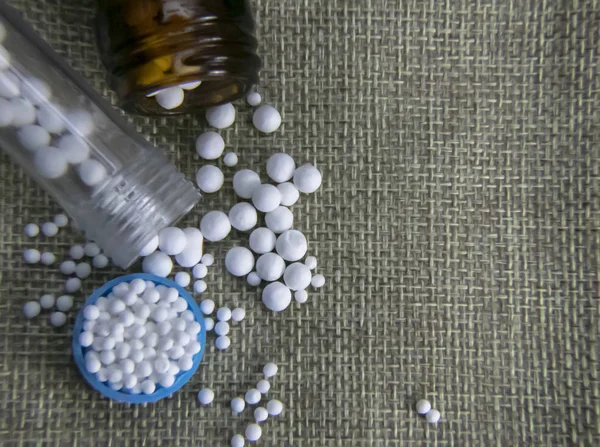 Close-up image of Scattered homeopathic globules and medicine bottles on jute sack background