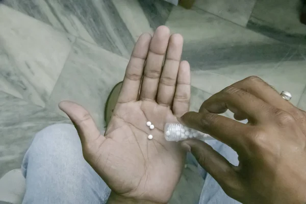 Eldeki şişeden homeopatik hap döken adamın yakından görünümü. Homeopatik ilaç günlük doz alarak erkek ellerin üst görünümü.
