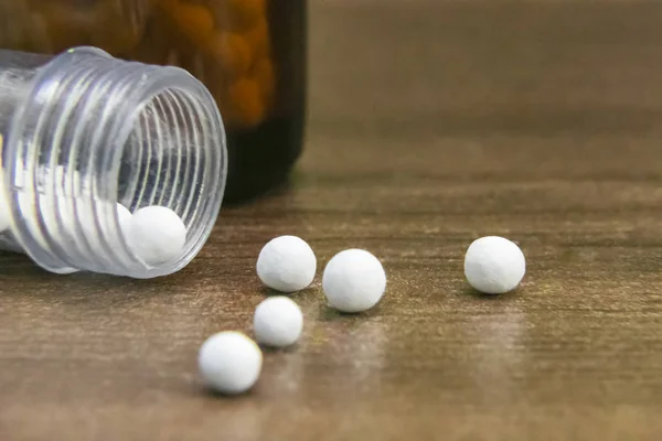 Homeopathic medicine bottle consisting of white pills scattered on wooden surface