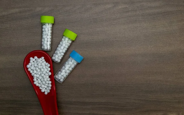 Top view image of homeopathic medicine consisting of the globules in red spoon and bottles containing pills on wood background