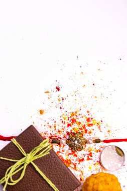 Hint festivali - Dağınık pirinçli şık Rakhi, kumkum ve haldi beyaz arka planda kahverengi hediye kutusu ve tatlı