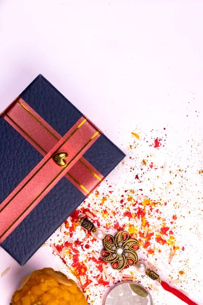 Indian festival of brother and sister - Rakhi and sweet with scattered rice, kumkum and haldi on white background with a beautiful gift box.