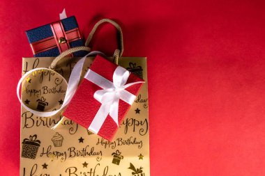Doğum günü hediyesi konsepti. Kurdeleli kırmızı ve mavi hediye kutuları ve kırmızı arkaplanda doğum günü mesajları olan çanta.