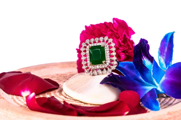 Side view of Emerald ring on oyster shell with decorated blue gift box and blue orchid flower and rose petals on white background with copy space in Jewellery gift concept