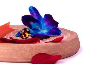 Yüzük hediye konsepti. Gül yaprakları ve beyaz arka planda mavi orkide çiçekleri olan kehribar taşı bir yüzük.