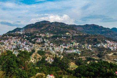 Arkaplanda bulutlu gökyüzü ve dağ aralığı ile geniş şehir manzarası