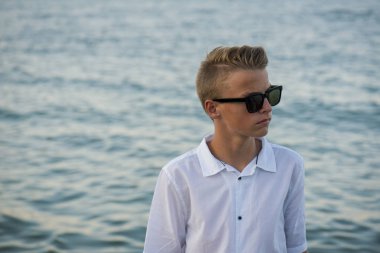 Zengin görünümlü bir çocuk arkasında deniz olan bir tatil yerinde..