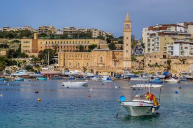 Marsascala Parish Kilisesi ve Marsaskala körfezinde geleneksel Malta balıkçı tekneleri (Luzzu) görünümü