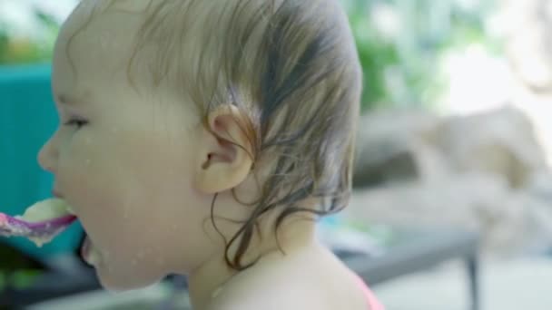 1歳の女の子はヤシの木、熱帯、スローモーションの近くの自然の中でお粥のスプーンを食べる — ストック動画