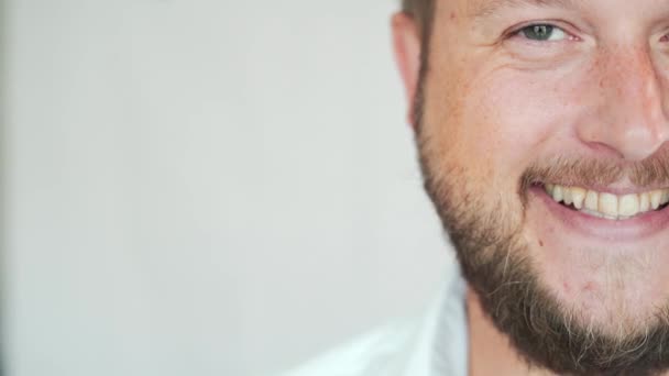 Bonito homem caucasiano com uma barba sorrindo em um fundo branco, retrato de um homem meio rosto . — Vídeo de Stock