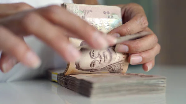 タイのバーツのお金の数える手を閉じます。クローズアップ人間カウントタイ紙幣、金持ちカウントと100を保持します。テーブルの上のバーツ紙幣. — ストック写真
