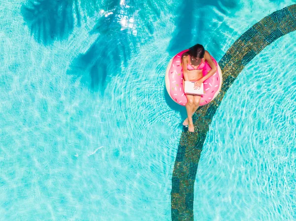 Young female freelancer sitting with a tablet in an inflatable circle in the pool. Aerial view — ストック写真