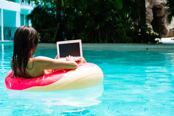 Meisje in de opblaasbare cirkel in het zwembad met een laptop, het concept van Freelancing en recreatie. — Stockfoto