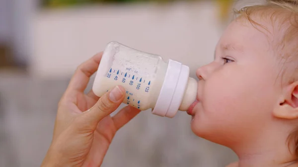 Søt jente som drikker melk fra en flaske i hagen. – stockfoto