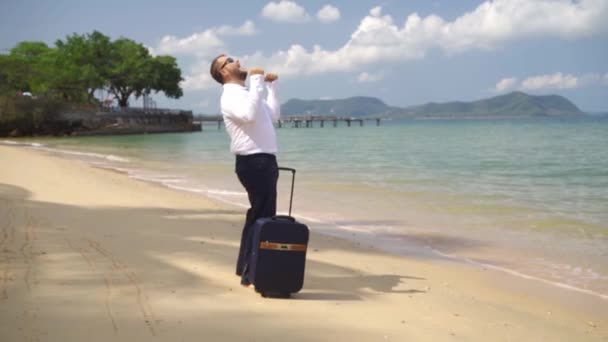 Homem de negócios caminha ao longo da costa de um belo mar com uma mala. férias felizes masculinas. conceito freelance, conceito de lazer tão esperado — Vídeo de Stock