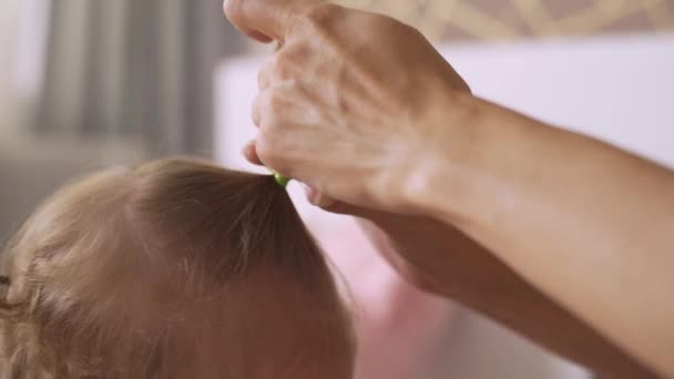 Мама робить своє маленьке волосся дочки, зв'язуючи волосся в хвостах — стокове відео