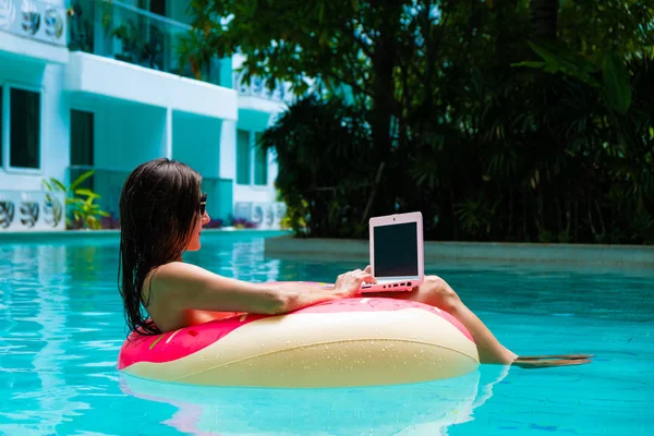 Meisje in de opblaasbare cirkel in het zwembad met een laptop, het concept van Freelancing en recreatie. — Stockfoto