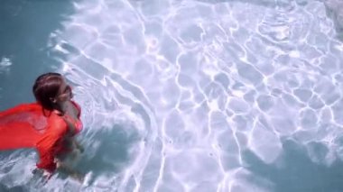 Pembe uzun elbiseli güzel kız havuzda yüzüyor. Pembe uzun elbiseli büyüleyici esmer mavi bir havuzda kamera için poz.