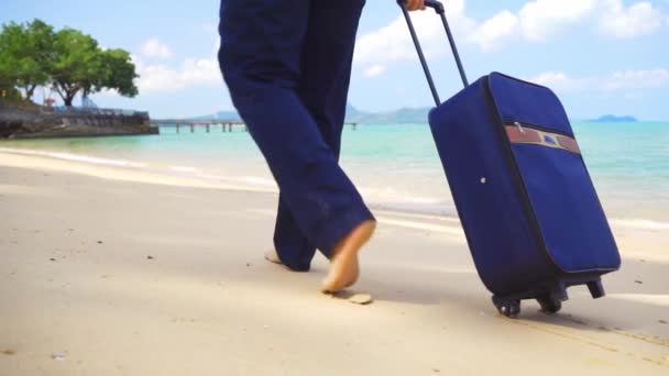 Affärsman ben går längs stranden av ett vackert hav med en resväska. frilans koncept, efterlängtat fritids koncept — Stockvideo