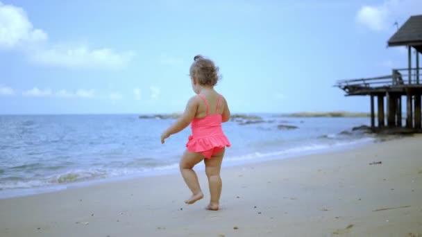Маленькая девочка в розовом купальнике бежит вдоль прекрасного пляжа . — стоковое видео