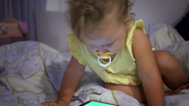 Klein meisje met mobiele telefoon in bed in de avond. Telefonische verslaving bij kinderen. — Stockvideo