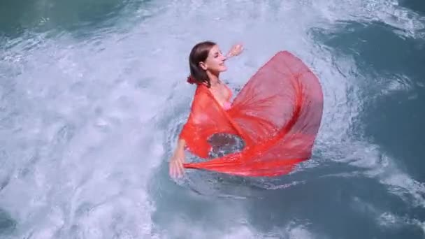 Krásná dívka v růžových dlouhých šatech plave v bazénu. Kouzelná bruneta v růžovém dlouhém oděvu představuje fotoaparát v modrém bazénu. — Stock video